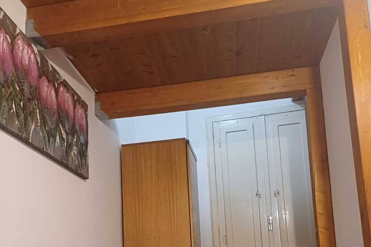A bedroom with a bed, wooden wardrobe, and a door leading to another room.