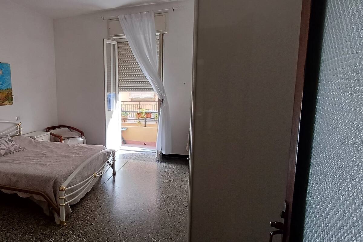 A bedroom with a bed, a nightstand, a painting, and a view of the outside.