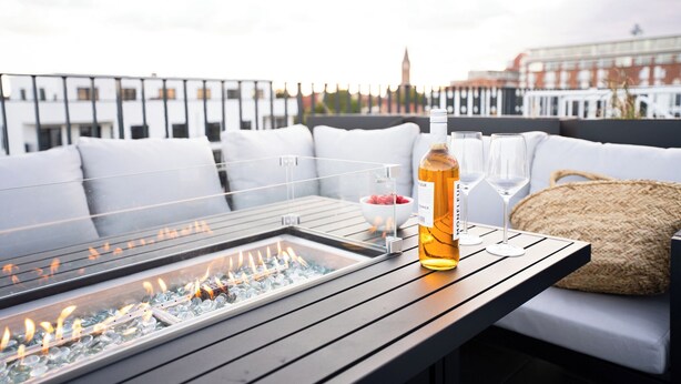 Una terraza en la azotea con una mesa de vidrio, una botella de licor y vasos.