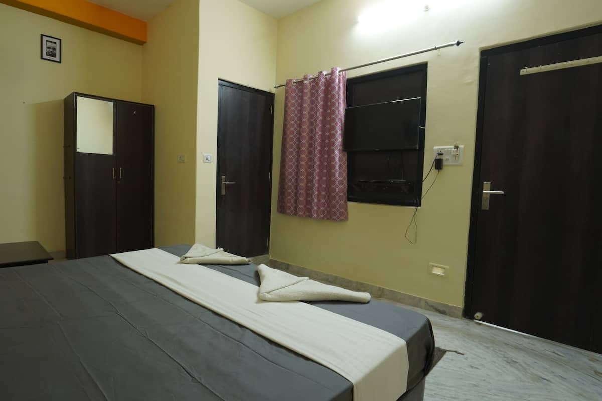 A hotel room with a bed, a wardrobe, a mirror, a window with a curtain, and a wall socket.