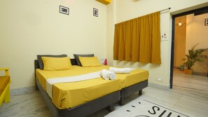 A hotel room with a bed, two pillows, a white towel, a yellow curtain, and a potted plant. - Hotel Kishangarh Jaisalmer (Jaisalmer)