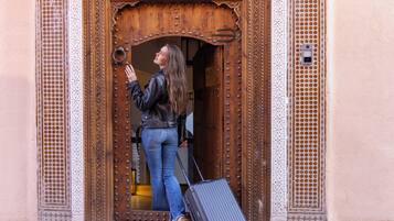 A woman standing at a wooden door with intricate carvings, holding a suitcase.