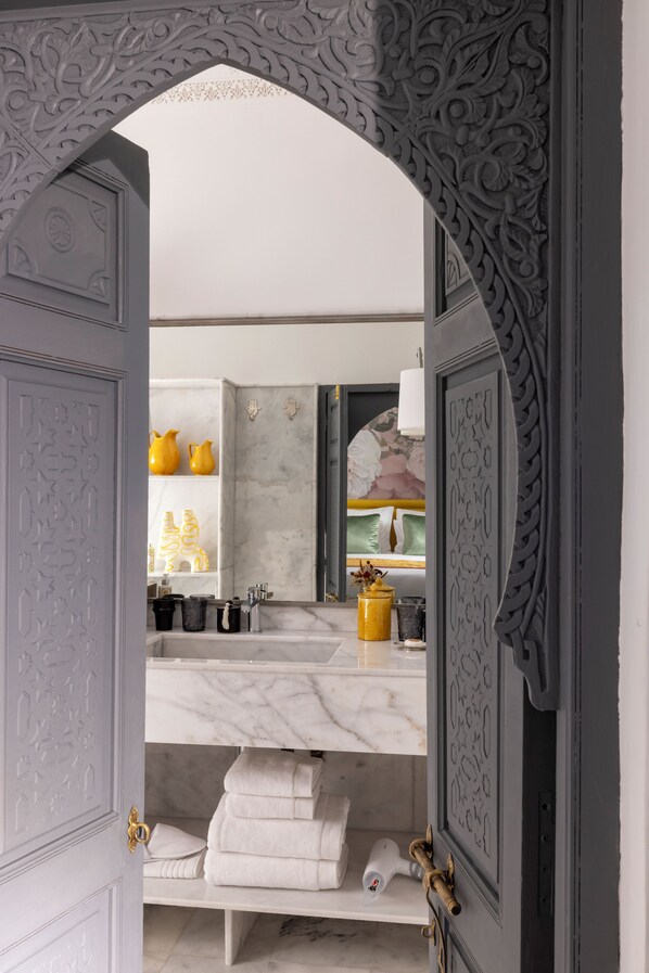 An ornate doorway leading to a bathroom with a marble sink, yellow vases, and neatly folded towels.
