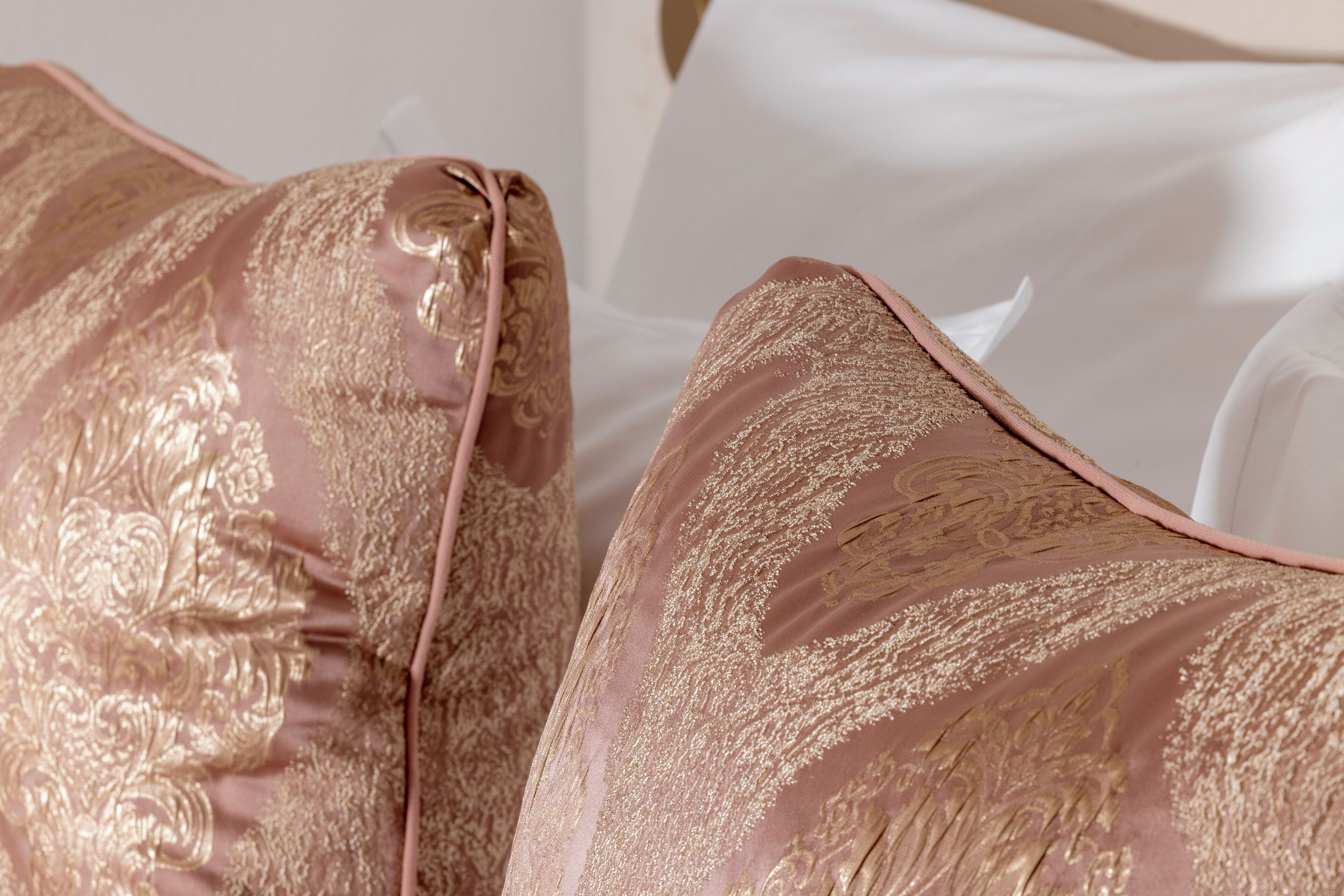 A close-up of a bed with a white sheet and two pink pillows with gold embroidery.