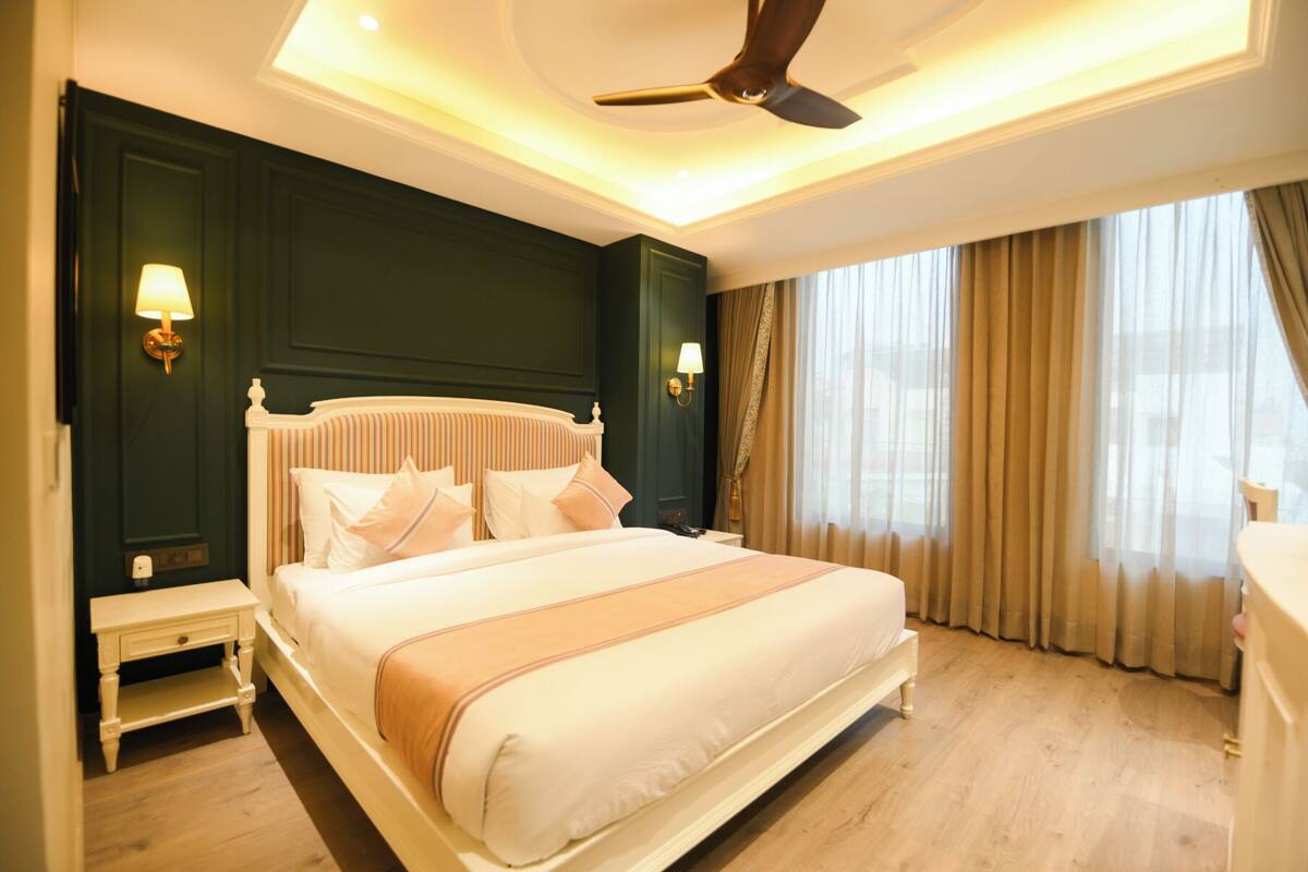 A hotel room with a large bed, a ceiling fan, two bedside lamps, a nightstand, and a window with curtains.