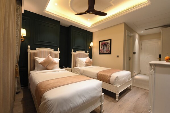 Habitación de hotel con dos camas, ventilador de techo, un cuadro y una pequeña cocina.