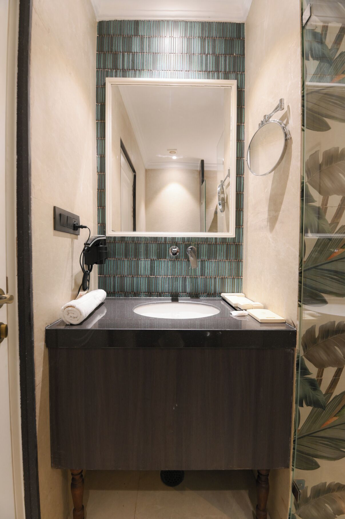 Une salle de bain avec un meuble-lavabo en bois foncé, un lavabo blanc et un miroir au-dessus. Il y a une serviette sur le comptoir et un sèche-cheveux branché.