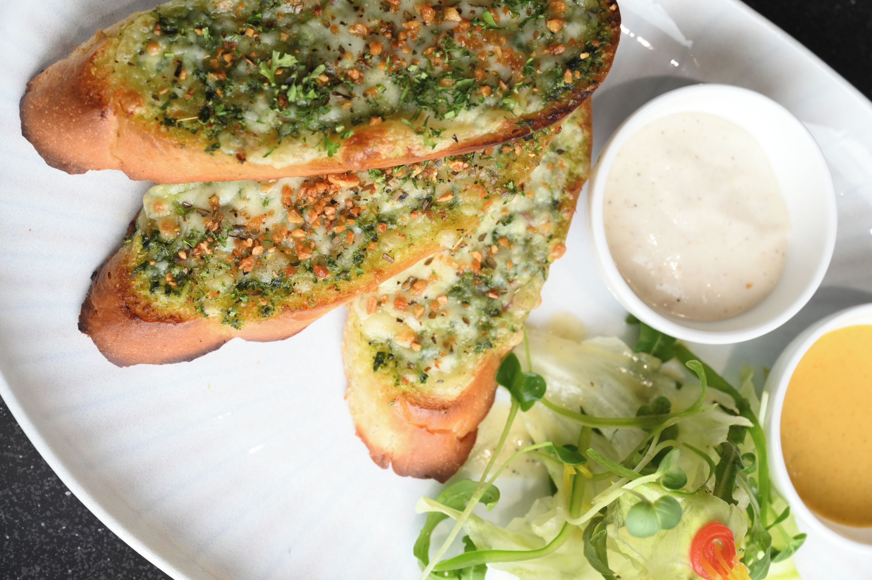 A plate with garlic bread, a salad, and two dipping sauces.