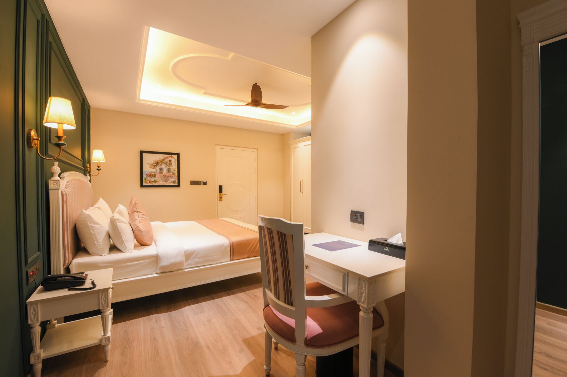 Quarto de hotel com cama, mesa de cabeceira, cadeira, escrivaninha e ventoinha no teto.