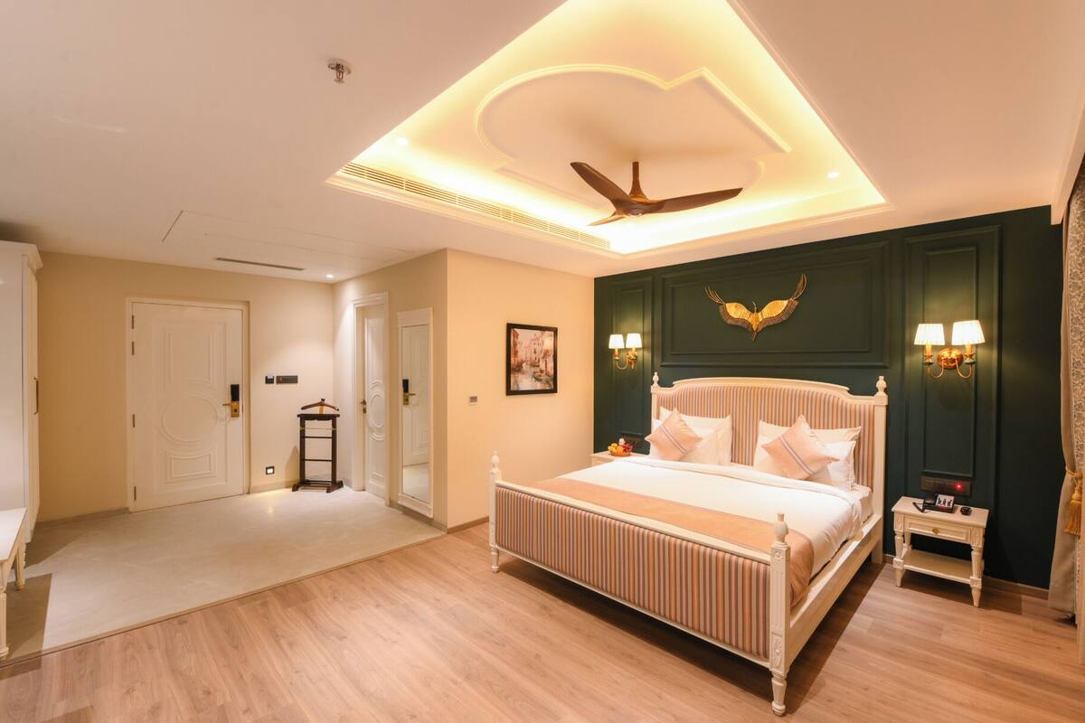 A hotel room with a large bed, a ceiling fan, a nightstand, and a wall-mounted lamp.