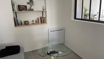 Ein modernes Wohnzimmer mit Glastisch, einer Couch, einer Heizung und einem Fenster mit Blick auf die Straße.