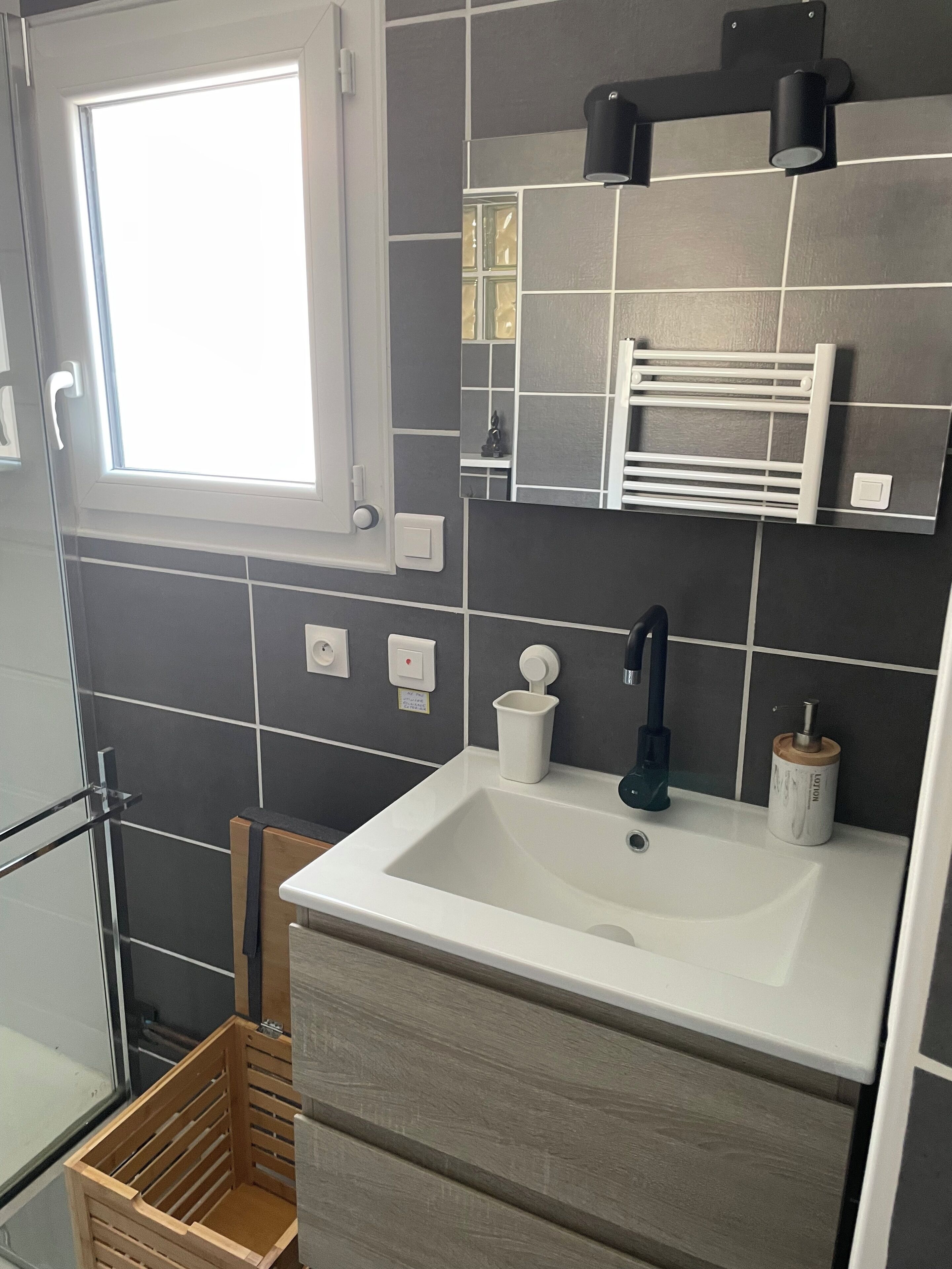 Een badkamer met een wit wastafelmeubel, een spiegel, een handdoekrek en een raam.