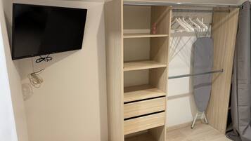 A room with a built-in wooden wardrobe, a flat-screen TV mounted on the wall, and a clothing rack with hangers.