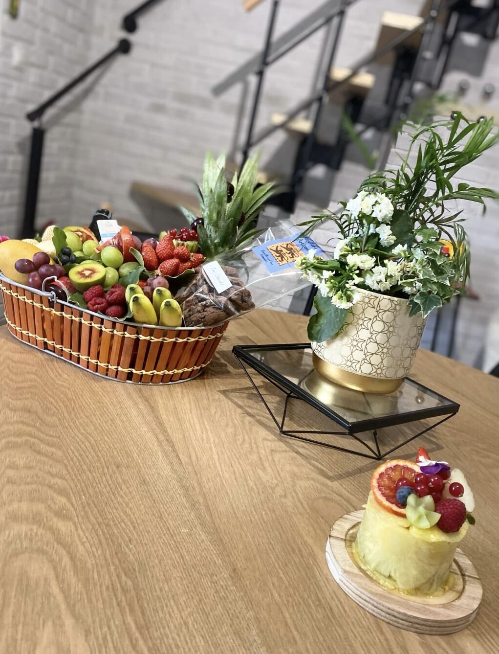 Une table en bois avec un panier de fruits, une plante en pot et un dessert.
