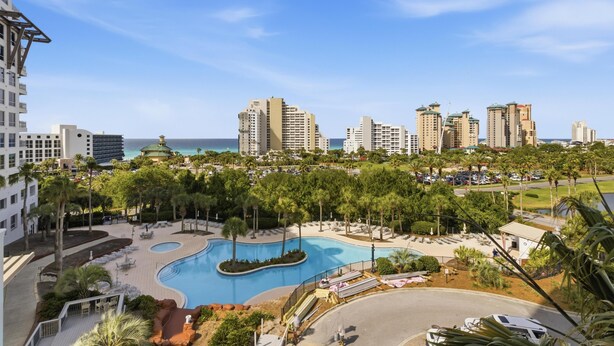Un resort con piscina, palmeras y edificios altos al fondo.