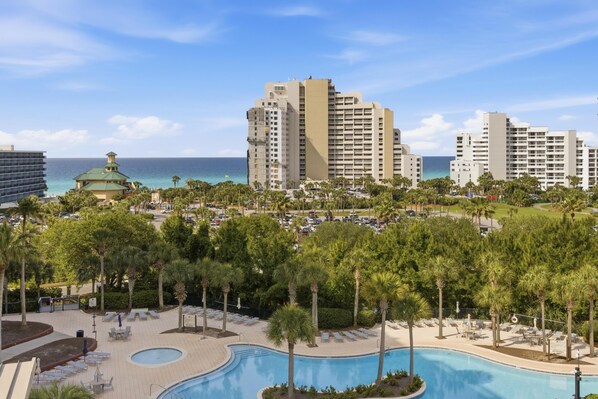 A resort with a swimming pool, palm trees, and beachfront buildings.