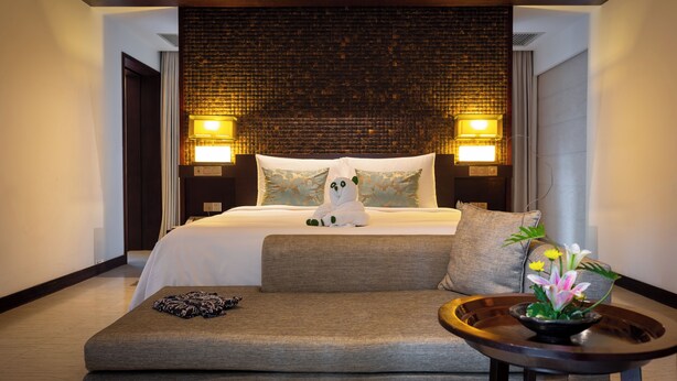 Een hotelkamer met een groot bed, twee bedlampen, een bank en een kleine tafel met bloemen.