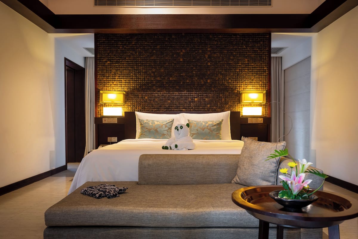 A hotel room with a large bed, two bedside lamps, a sofa, and a small table with a flower arrangement.