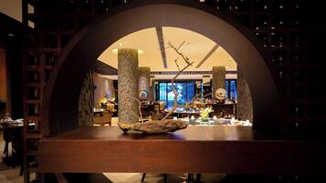 A modern interior with a central wooden table, a decorative branch, and a circular arch framing the view.