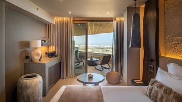 A modern hotel room with a large bed, a small table, a chair, a sofa, a large vase, a lamp, and a view of the city through the balcony.