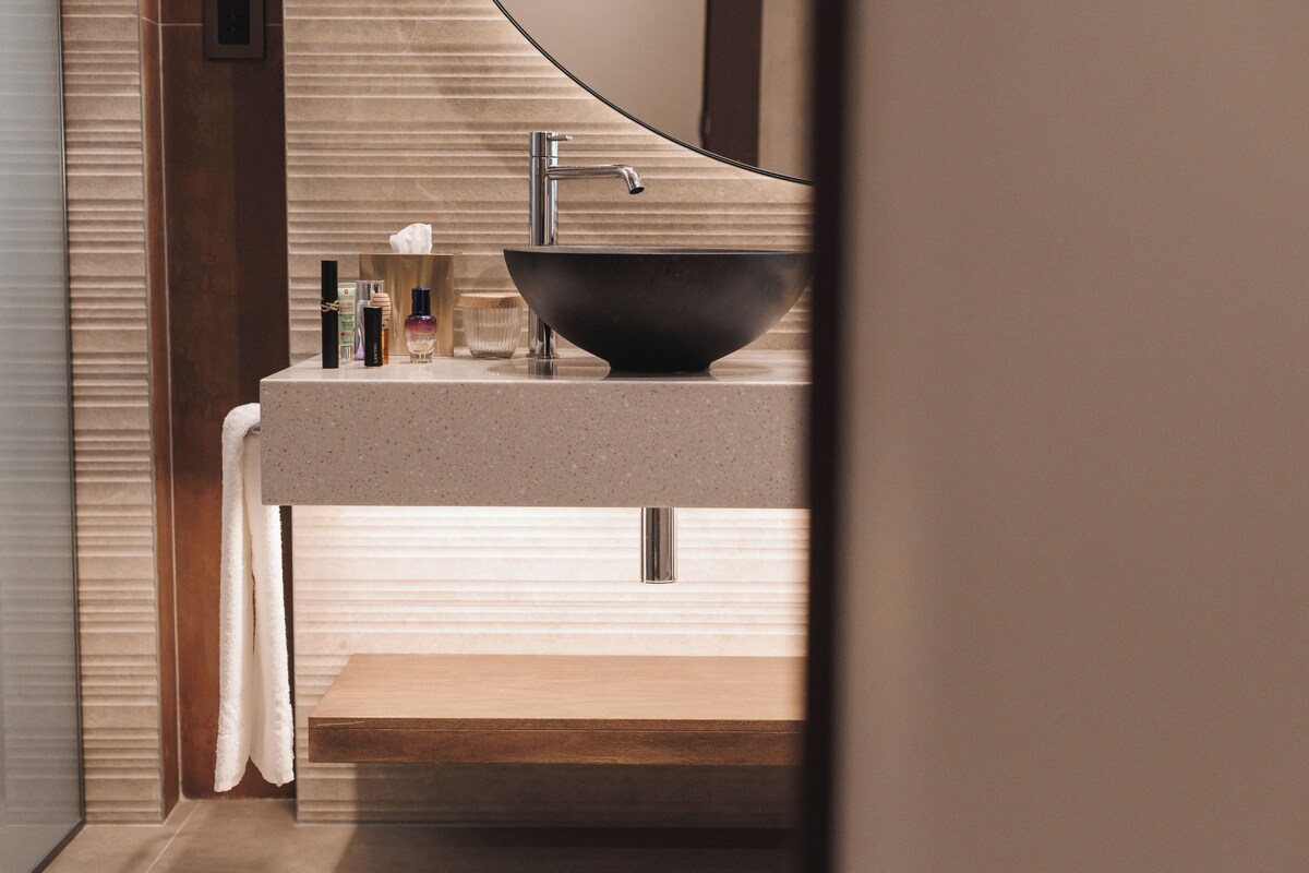 Een moderne badkamer met een grote, donkere wastafel, een houten wastafelmeubel, en een handdoek aan een handdoekhouder.
