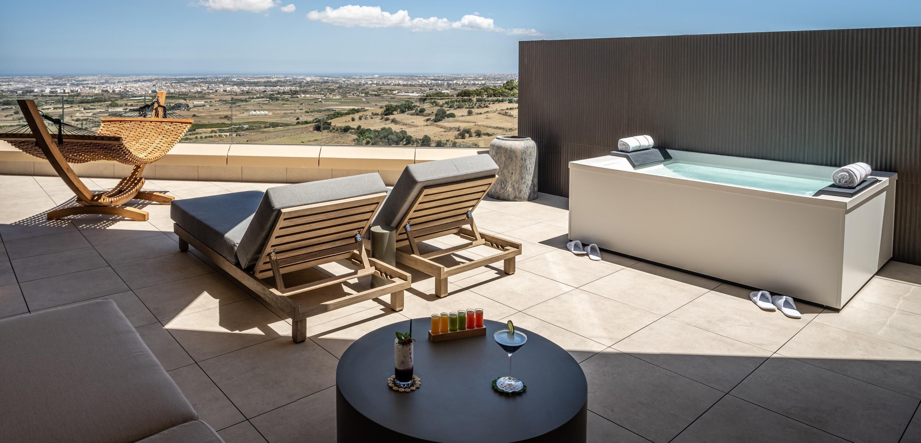 Een terras op het dak met een jacuzzi, lounge fauteuils en een tafel met drankjes.
