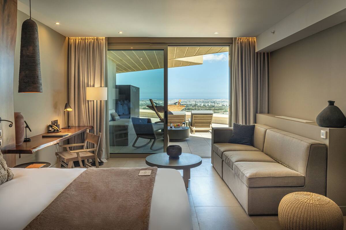 Une chambre d’hôtel moderne équipée d’un lit, d’un canapé, d’un bureau et d’un balcon avec vue.