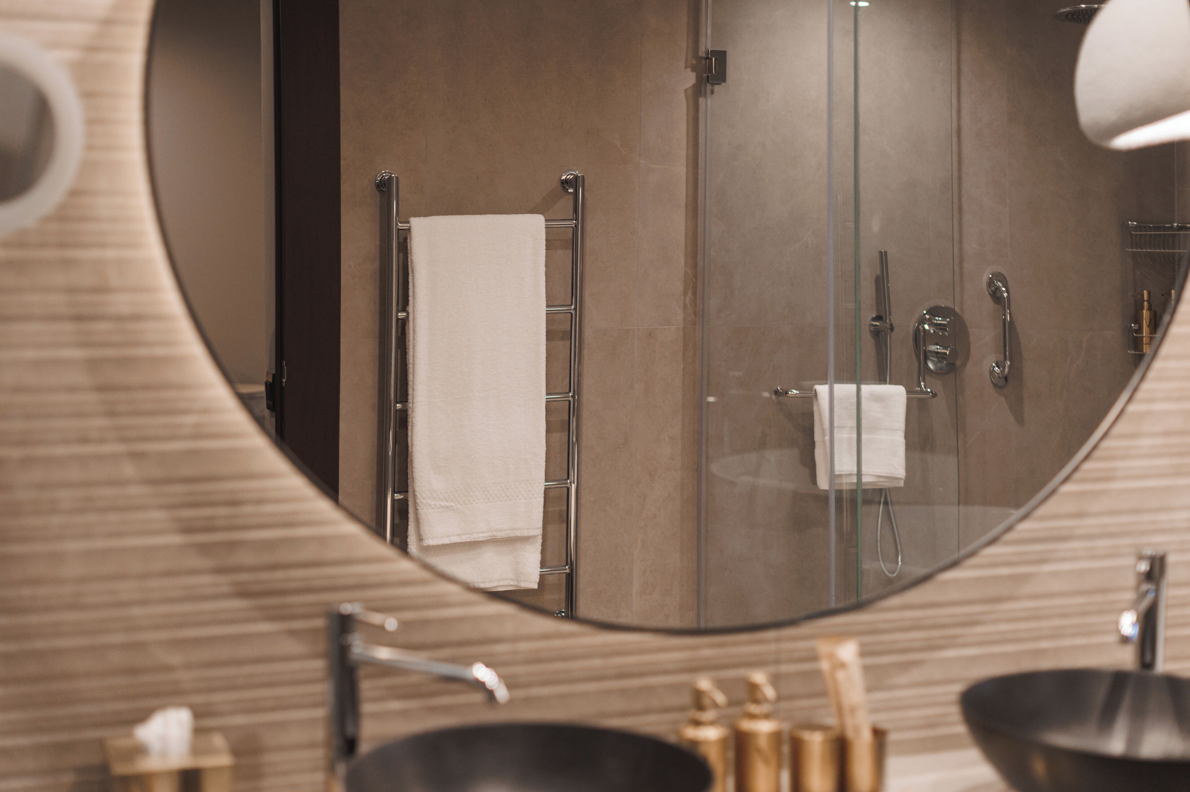 A modern bathroom with a round mirror, a towel rack, a glass shower enclosure, and a black sink.