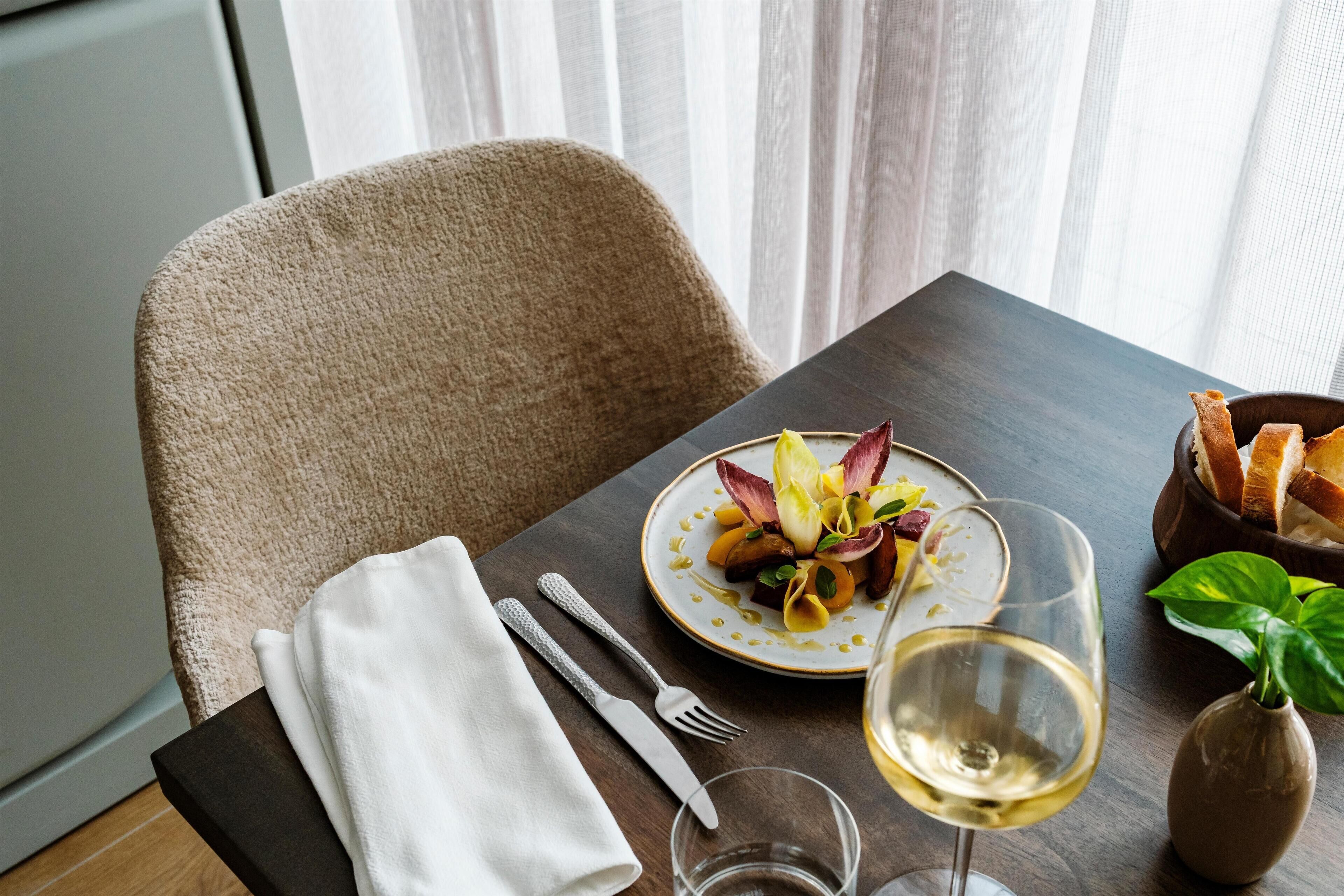 Une table à manger avec une assiette de nourriture, un verre de vin, des couverts et une serviette.