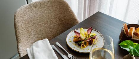 A dining table with a plate of food, a glass of wine, cutlery, and a napkin.