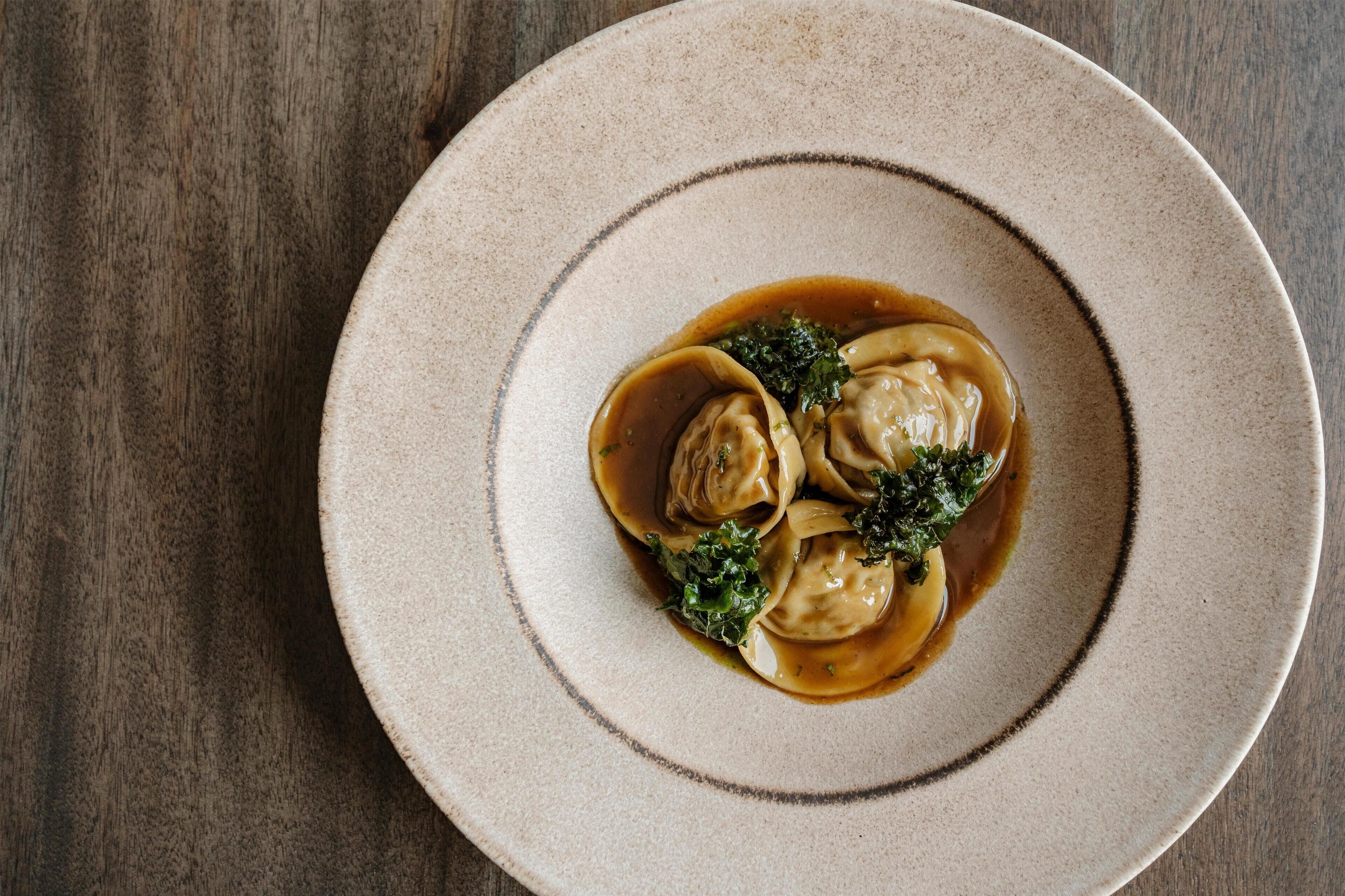 A plate of dumplings with a sauce and greens on a wooden table.