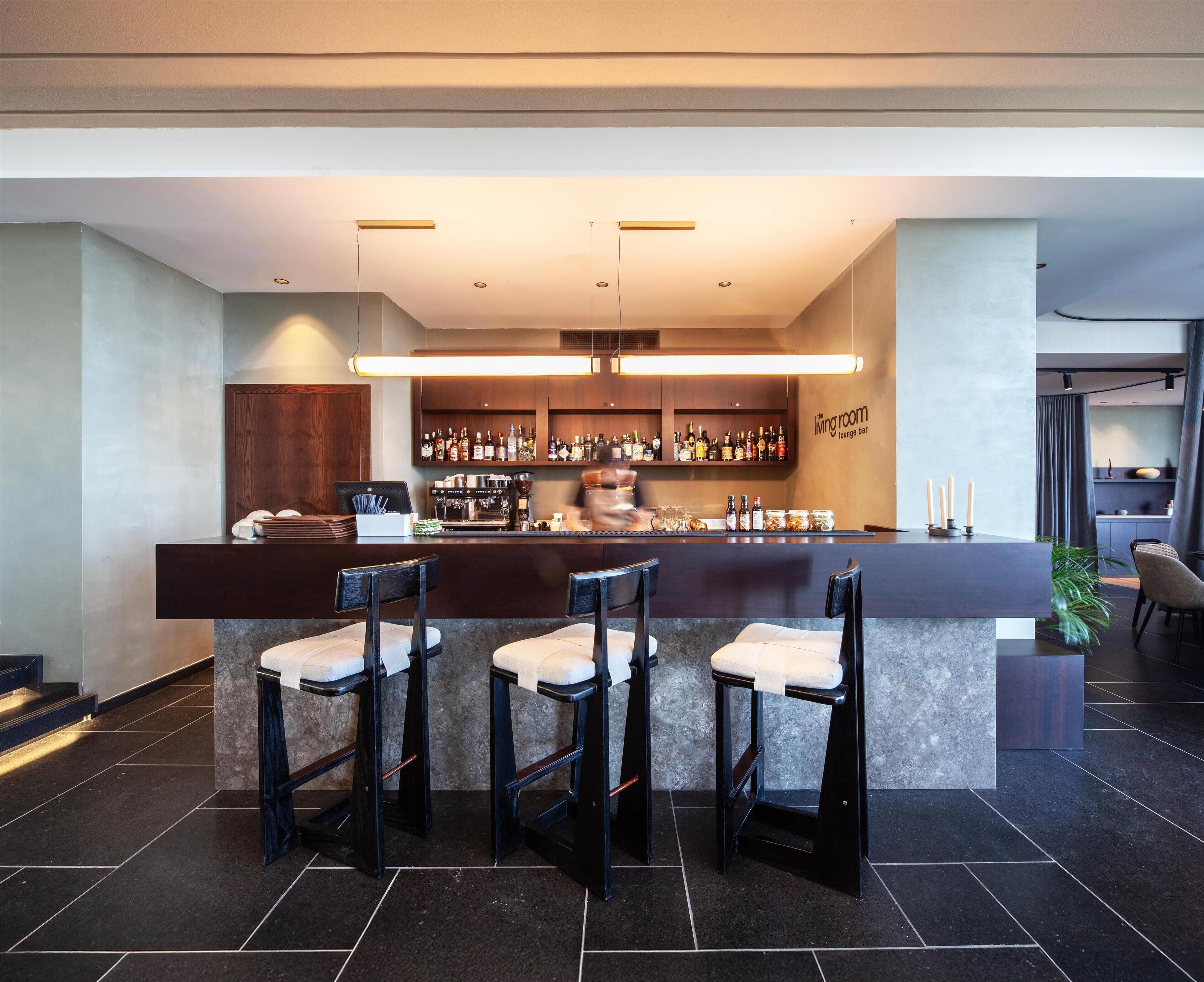 Zona de bar moderna con una barra alargada, varios taburetes y una amplia selección de botellas y vasos.