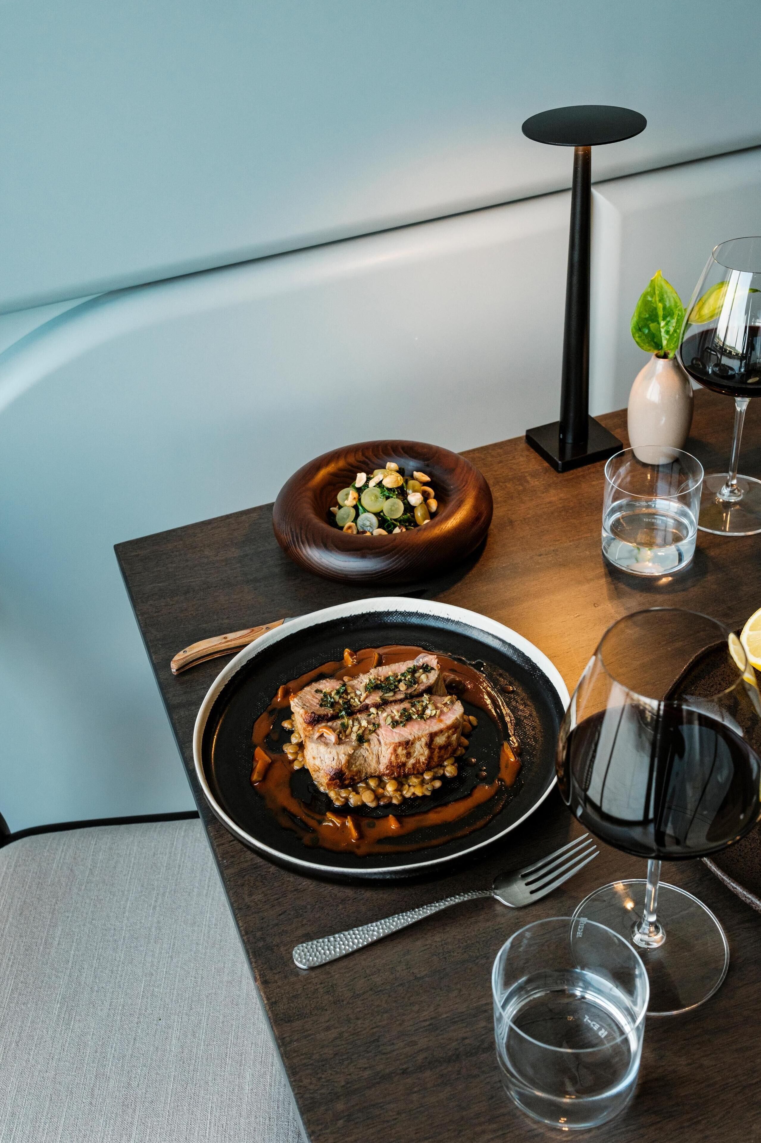 A dining table with a plate of food, a bowl of salad, and a wine glass.