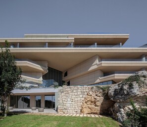 Un edificio moderno a più piani con tetto piano, ampie finestre e un muro di sostegno in pietra.