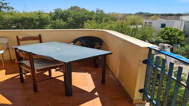 Un balcón con mesa y sillas, suelo de baldosas y barandilla azul.