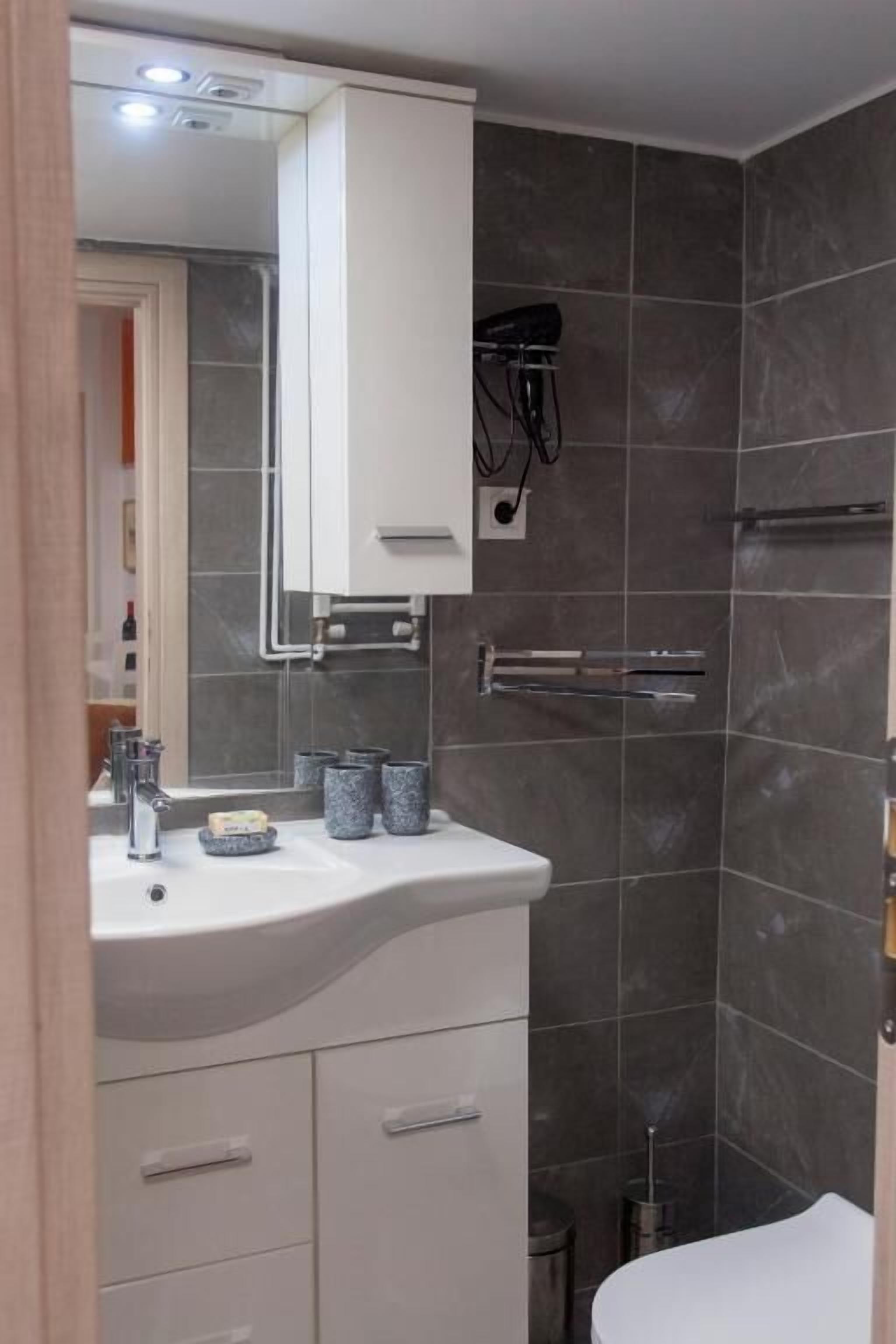 A modern bathroom with a white vanity, dark tiled walls, a shower area, and a visible hairdryer.