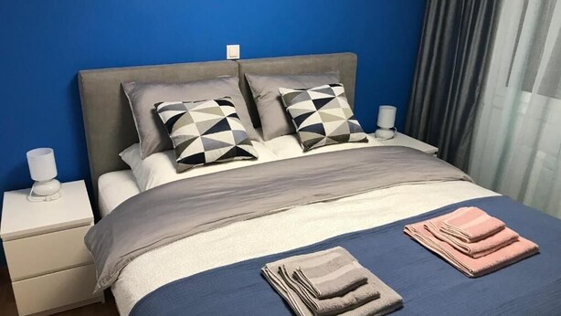 A neatly made bed with geometric patterned pillows, a blue and grey bedspread, and folded towels on the bed. - Ancient Thissio by GHH (Athens)