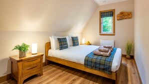 A bedroom with a wooden bed, a nightstand, a bedside table, a window with a view of greenery, and a wall-mounted decoration. - Wonderful private villa for 4 guests with WIFI, TV, balcony and panoramic view (Kilfinnan)