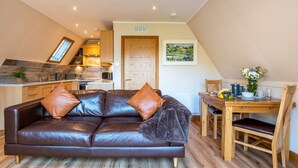 A cozy living area with a leather sofa, wooden dining table, and a kitchen in the background. - Wonderful private villa for 4 guests with WIFI, TV, balcony and panoramic view (Kilfinnan)