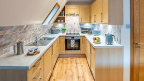 A modern kitchen with wooden cabinets, a tiled backsplash, and a built-in oven. - Stunning private villa for 4 guests with WIFI, TV, balcony and panoramic view (Kilfinnan)
