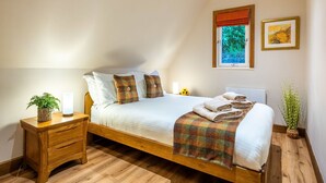 A bedroom with a wooden bed, white bedding, a small bedside table with a plant, a window with a view of greenery, and a framed picture on the wall. - Stunning private villa for 4 guests with WIFI, TV, balcony and panoramic view (Kilfinnan)
