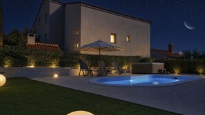 Een modern huis met zwembad, terras en een nachthemel met sterren en een maan.