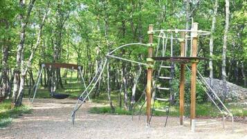 Explore the playground area surrounded by trees, featuring a swing set and climbing structure.