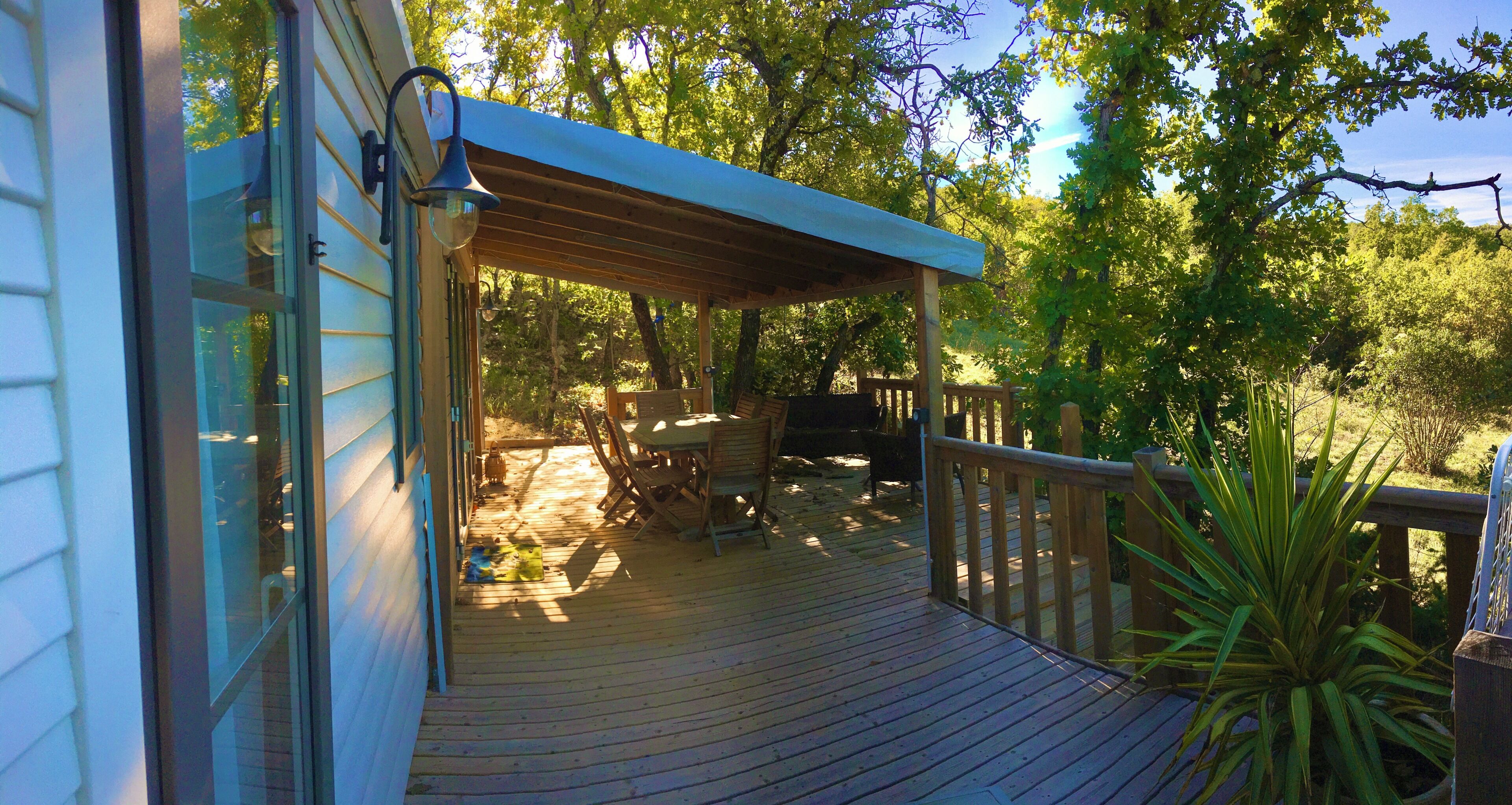 A wooden deck with a covered seating area, surrounded by trees.