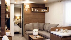 A compact living space with a sofa, a small table, a cabinet, and a doorway leading to a bedroom. - Domaine le Clos des Capitelles (Saint-Privat-de-Champclos)