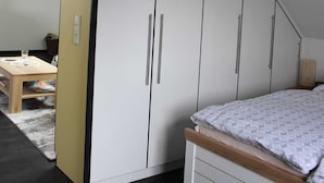 A bedroom with a sloped ceiling, a bed with a patterned bedspread, and a wardrobe with multiple doors.