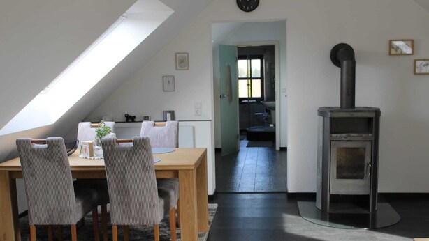 A dining area with a table and chairs, a black stove, and a skylight.