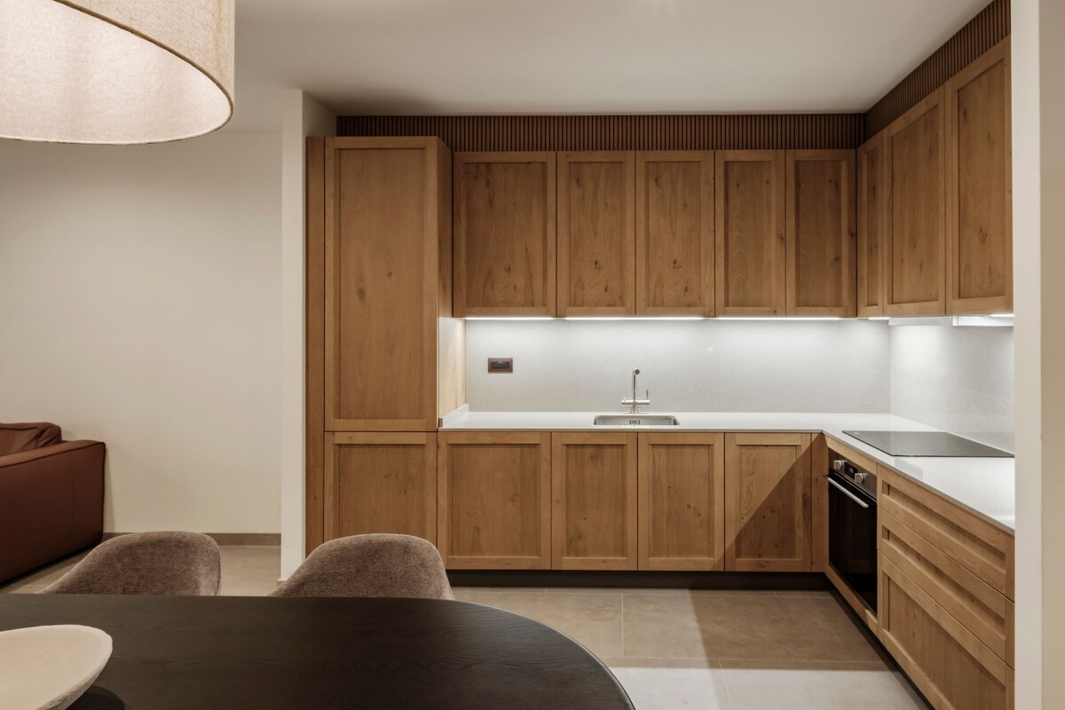 A modern kitchen with wooden cabinets, a white countertop, and a dining area with a table and chairs.
