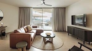 Un salon moderne comprenant un canapé, une table basse, un téléviseur et un balcon aménagé avec du mobilier d’extérieur.