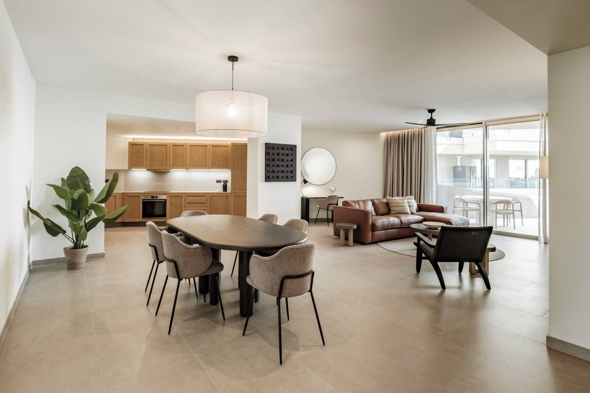 A spacious living area with a dining table, sofas, and a large window offering a view of the city.